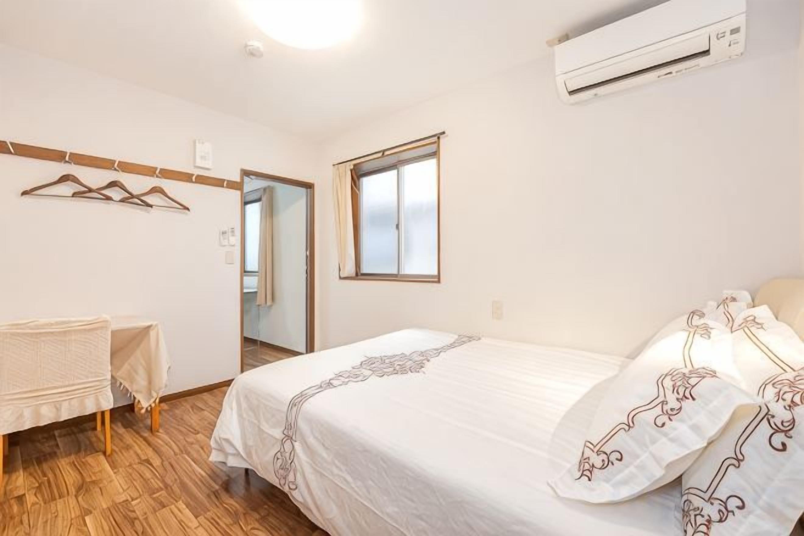A bedroom with a bed, a bedside table, a hanging coat rack, and a window.