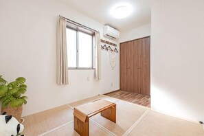A room with tatami flooring, a wooden bench, a potted plant, a window with curtains, and a wardrobe. - W.Hostel (Tokyo)