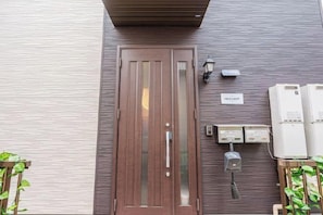 A door with a nameplate, a wall-mounted light, and electrical boxes. - W.Hostel (Tokyo)