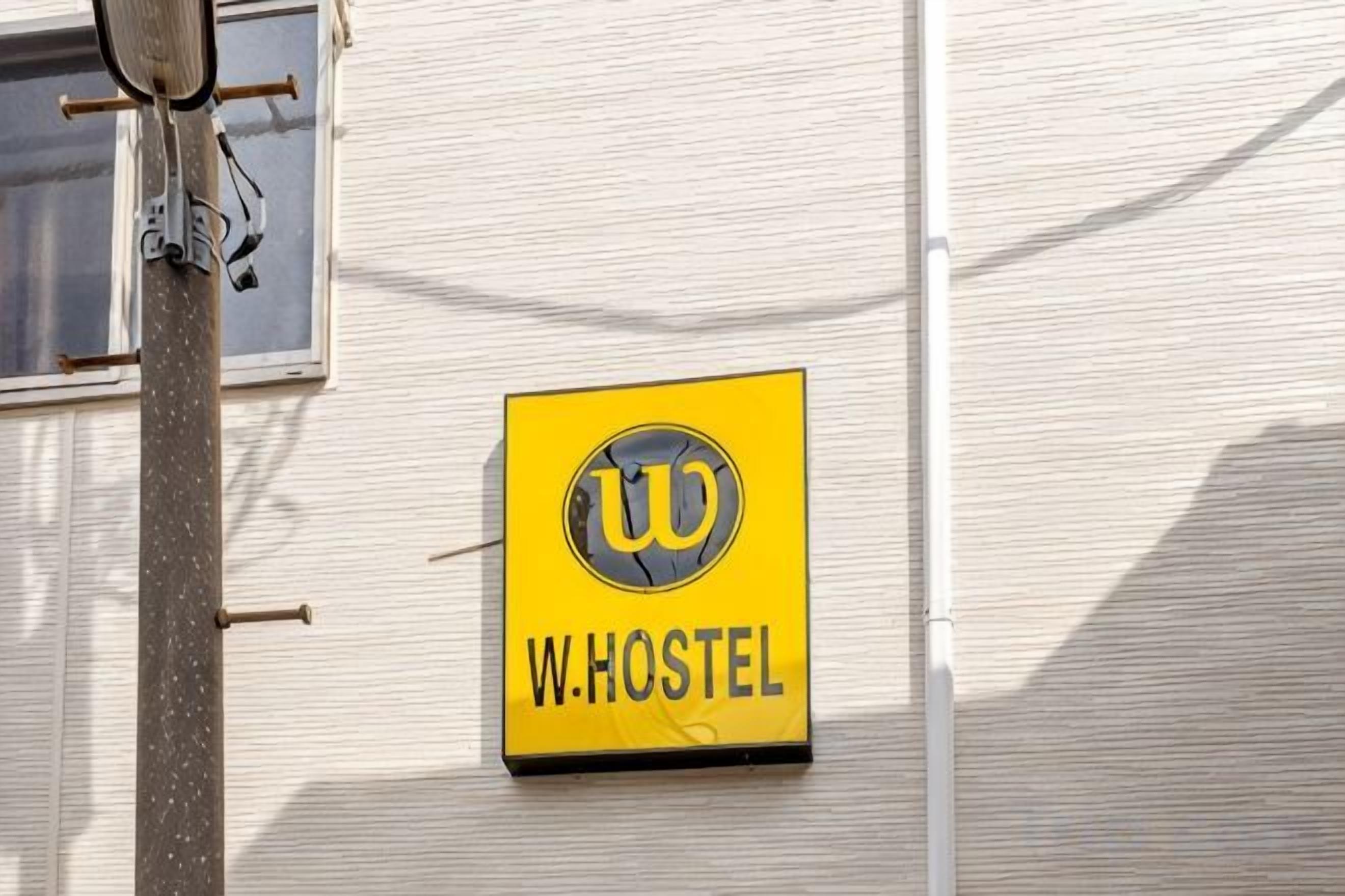 A yellow sign with a logo and the text 'W.HOSTEL' on a building facade.