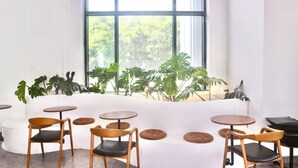 A modern interior with a white sofa, wooden chairs, and round tables. - Monstera Hotel and Coffee (Phu Quoc)