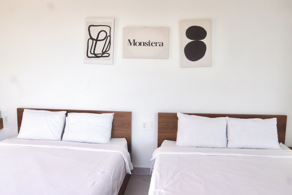 A hotel room with two beds, white bedding, a wooden headboard, and three wall art pieces.