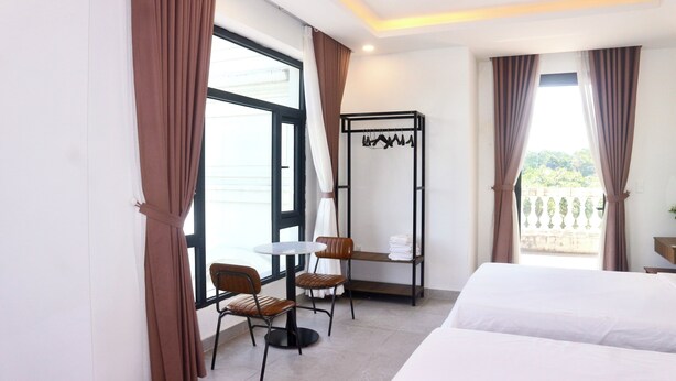 A hotel room with a bed, a small table, two chairs, a coat rack, and a balcony with a view. - Monstera Hotel and Coffee (Phu Quoc)