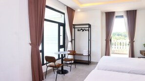 Ein Hotelzimmer mit Bett, kleinem Tisch, zwei Stühlen, Kleiderständer und einem Balkon mit Blick.