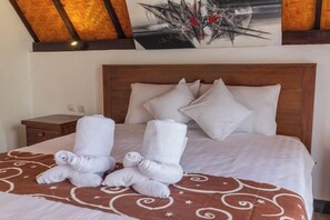A neatly made bed with white linens and rolled towels, a wooden headboard, and a brown patterned bedspread. - Maskot Penida Cottage (Bali)