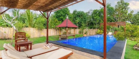A covered outdoor area with a pool, lounge chairs, and a gazebo.