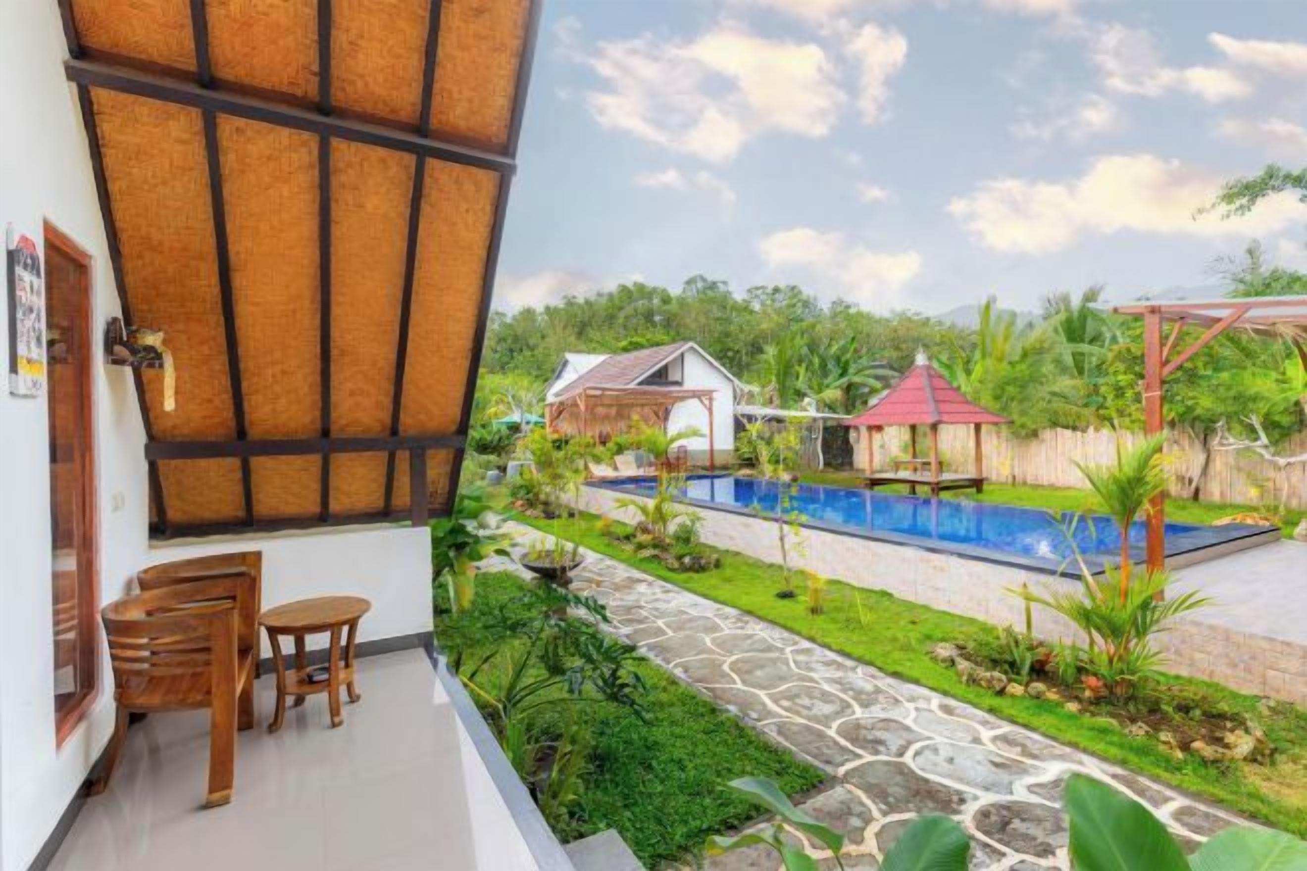 A balcony with a view of a swimming pool, a small garden, and a red-roofed structure.