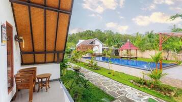 A balcony with a view of a swimming pool, a small garden, and a red-roofed structure.