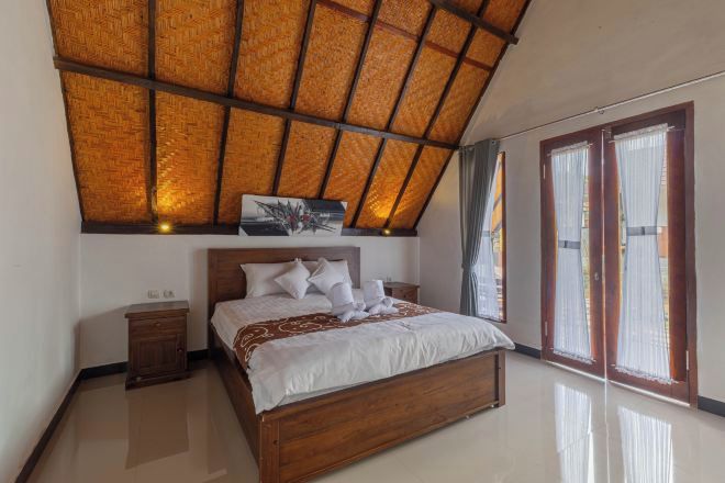 Un dormitorio con una cama de madera, una mesita de noche, un ventilador de techo y un gran ventanal con cortinas.