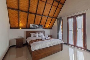 A bedroom with a wooden bed, a nightstand, a ceiling fan, and a large window with curtains. - Maskot Penida Cottage (Bali)