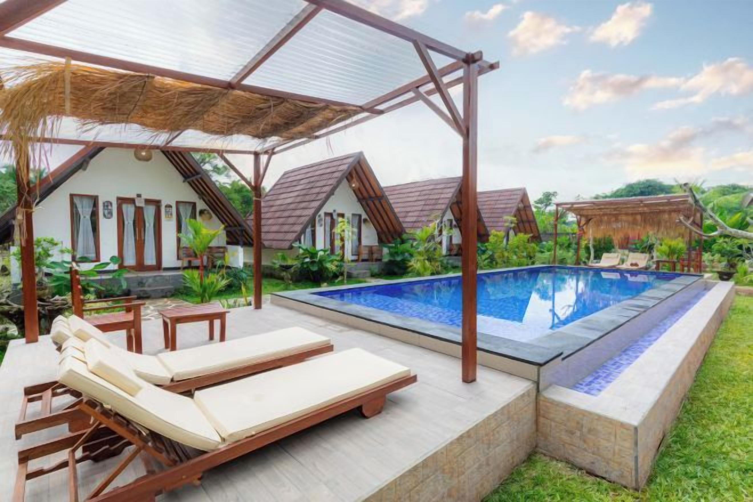 Área de piscina com espreguiçadeiras, um pérgola e vista para uma casa com telhado de palha.