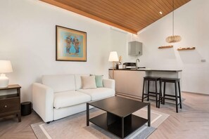 A modern living room with a sofa, coffee table, and kitchen area with stools. - The Lai Tiny House at Mae Kampong (Mae On)