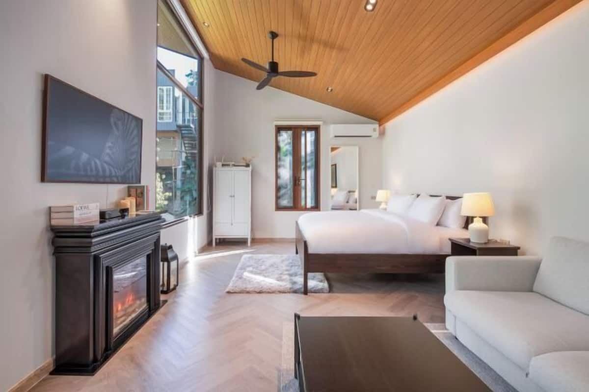 A modern bedroom with a large bed, a fireplace, and a ceiling fan.