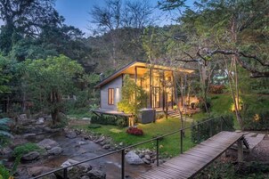 Una casa con terraza que da a un jardín y un arroyo.
