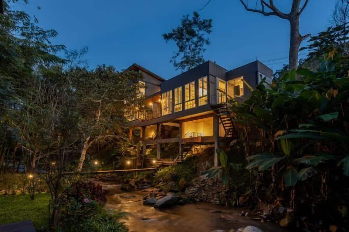 A modern house with a large balcony, a staircase, and a garden with a stream.