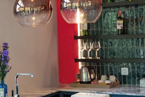A kitchen area with a marble countertop, a vase with flowers, a coffee maker, and a wine rack with glasses. - The Lai Tiny House at Mae Kampong (Mae On)