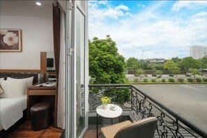 A hotel room with a bed, a small table with a vase, a chair, and a balcony with a view of trees and buildings. - Lam Anh Hotel 2 Duong Noi Ha Dong (Hanoi)