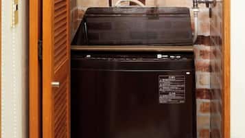 Ein kompakter, dunkel gefärbter Kühlschrank in einem Zimmer mit Backsteinwand und Holztür.