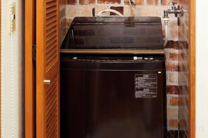 Un réfrigérateur compact, de couleur sombre, se trouve dans une pièce dont un mur est en briques et la porte en bois.