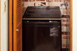 Un refrigerador pequeño y de color oscuro en una habitación con pared de ladrillo y puerta de madera.