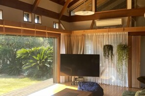 A room with a large flat-screen TV, a wooden ceiling, and a view of greenery outside. - Malama Monstera - In a botanical space, pls have a relaxing time. (Isumi)