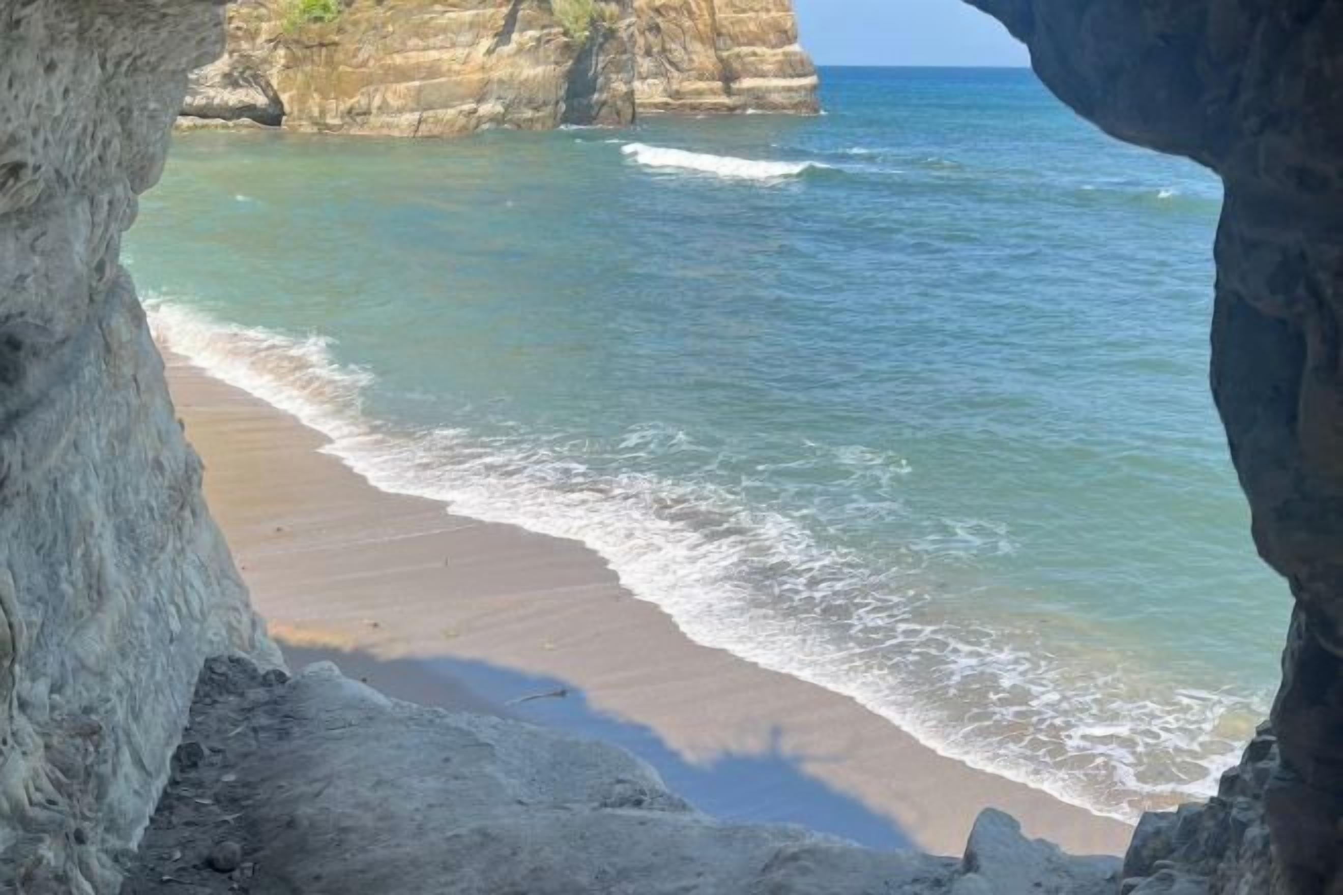Une plage à l’eau claire, une rive sablonneuse et une falaise rocheuse en arrière-plan.