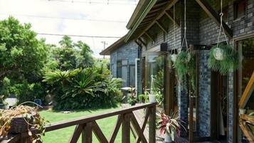 Una terraza de madera con barandilla, un edificio de ladrillo con puerta de cristal y plantas colgantes.