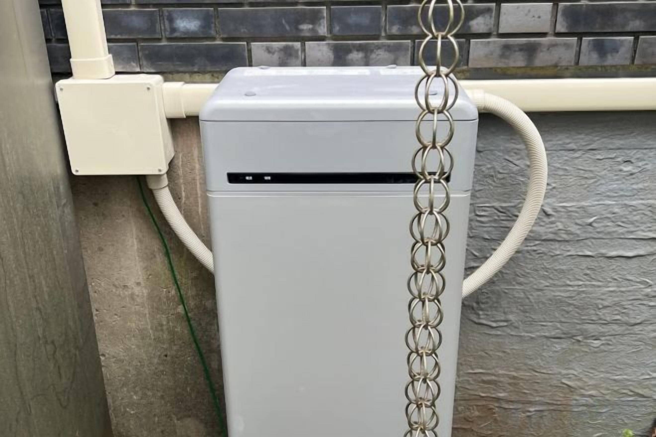 A white outdoor unit with a chain attached, connected to a hose.