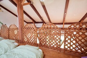 Una habitación con un marco de cama de madera, un separador de listones y un techo con vigas de madera.