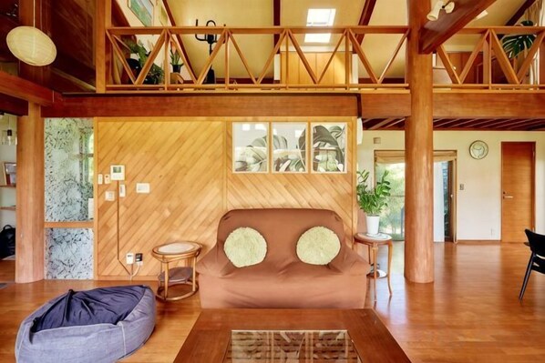 Un grand espace de vie doté d’un plafond en bois, d’un canapé avec des coussins, d’un fauteuil en forme de poire et d’une petite table.