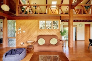 Amplia sala de estar con techo de madera, un sofá con cojines, un sillón de peluche y una mesita.
