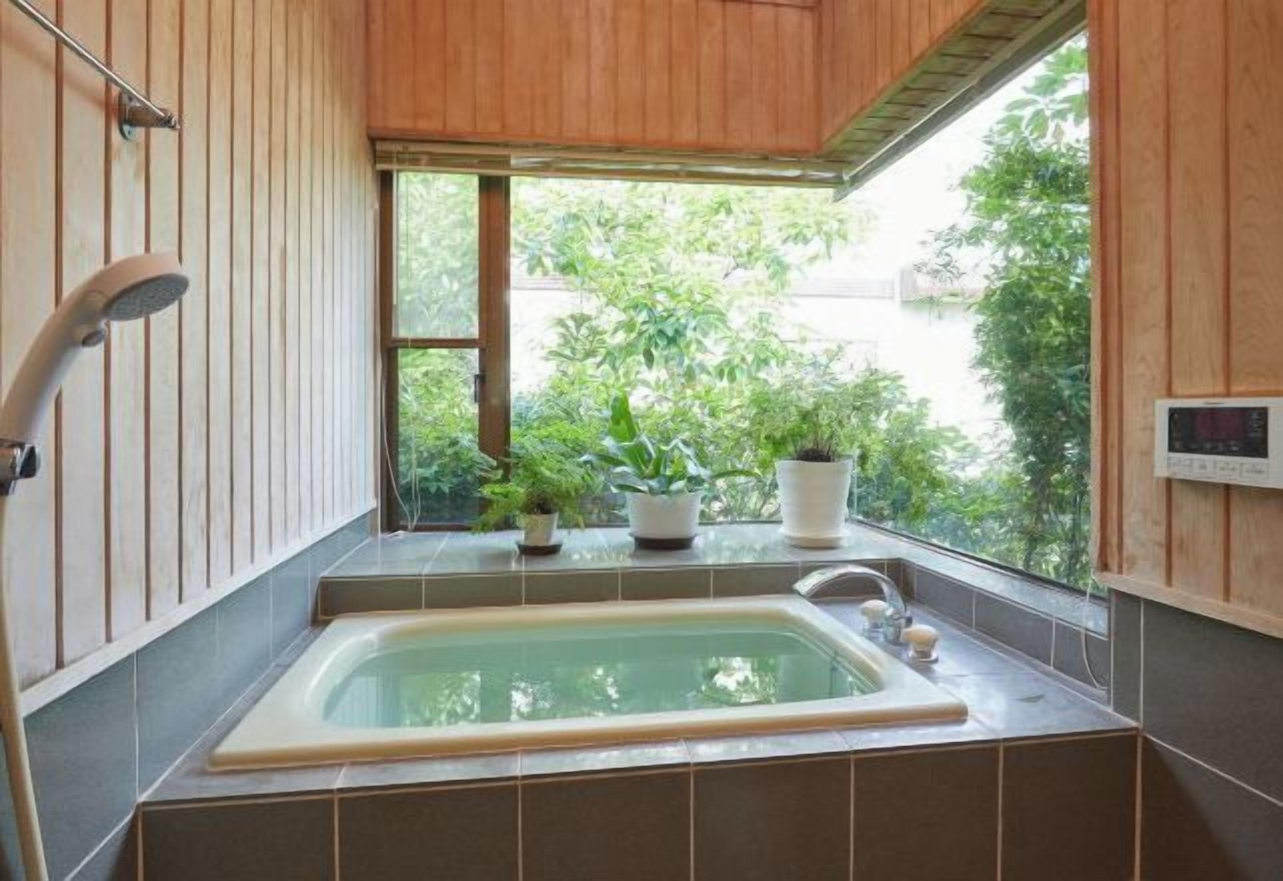 Een badkamer met een bad, houten wanden, een raam met uitzicht op groen en een potplant op de vensterbank.