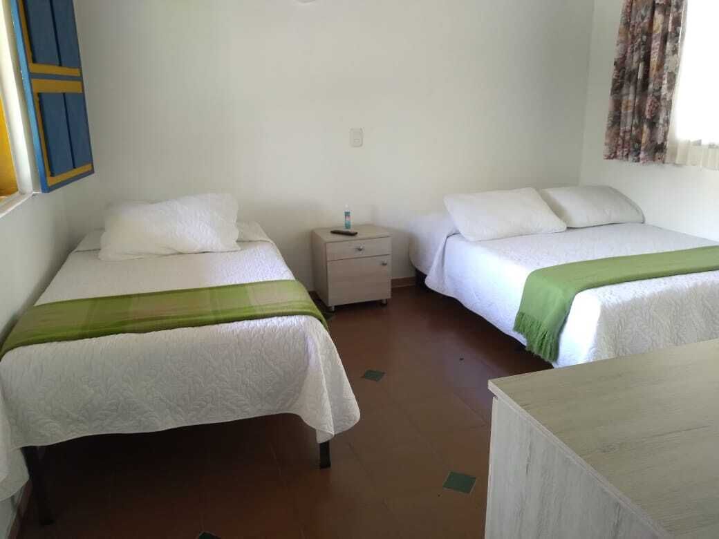 A room with two beds, each with white bedding and a green accent. There is a nightstand between the beds with a bottle on it.