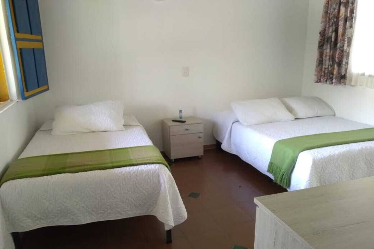 A room with two beds, each with white bedding and a green accent. There is a nightstand between the beds with a bottle on it.