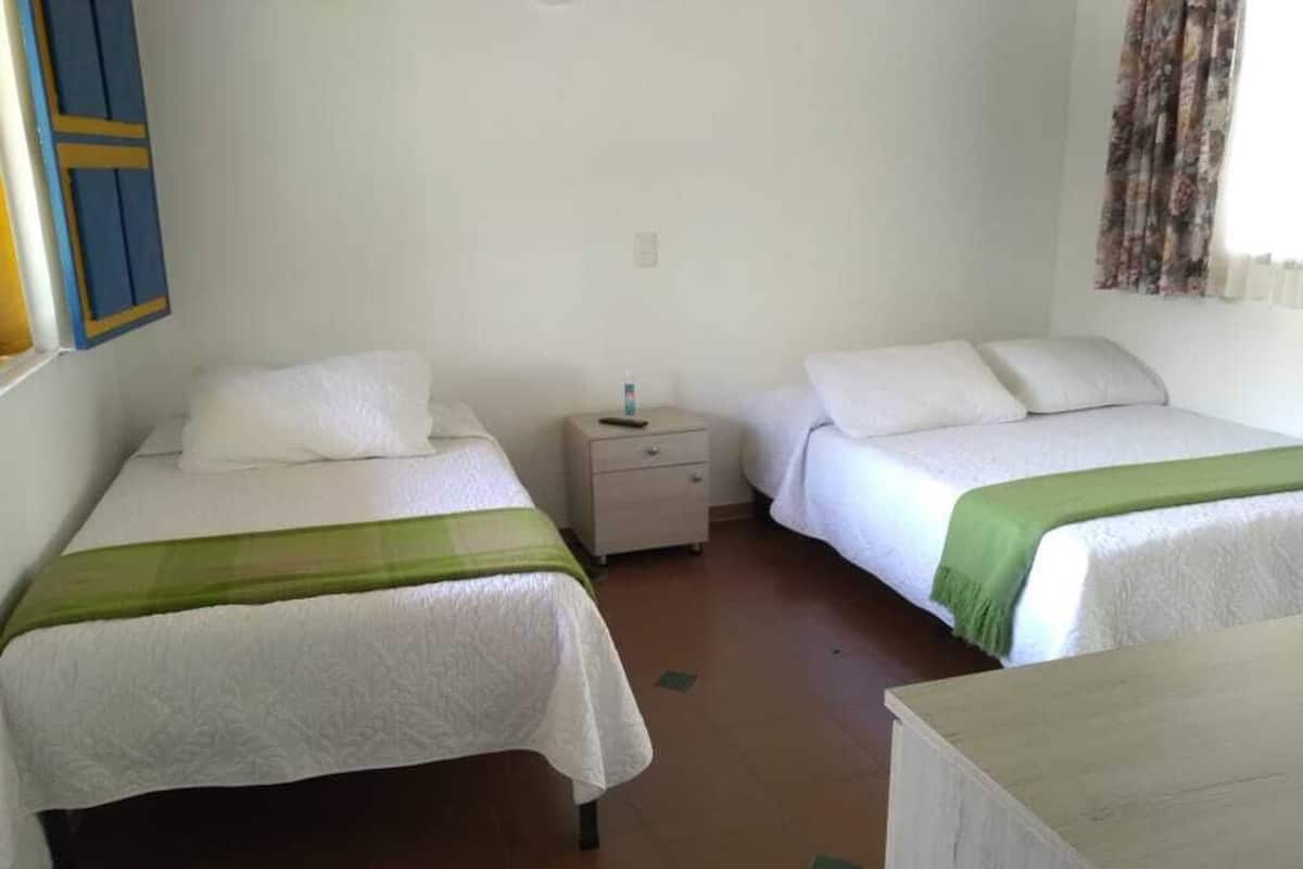 Ein Zimmer mit zwei Betten, jeweils mit weißer Bettwäsche und einem grünen Akzent. Dazwischen steht ein Nachttisch mit einer Flasche darauf.