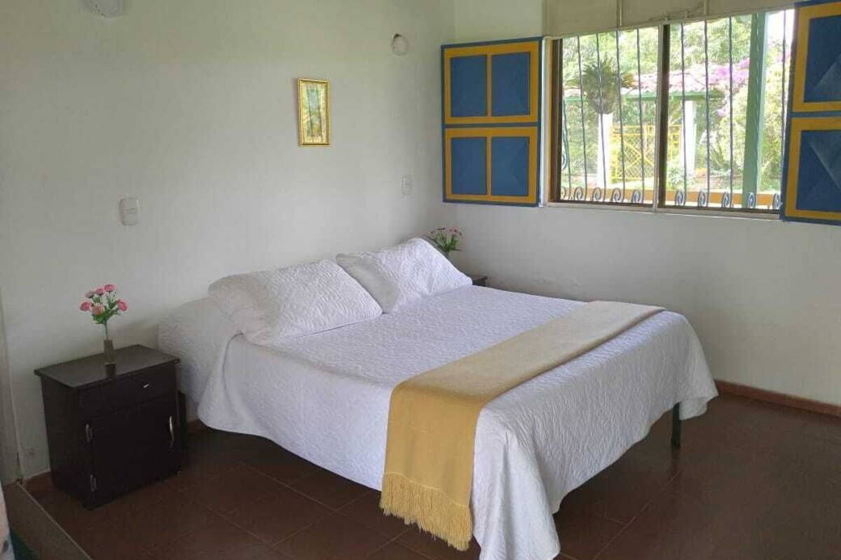 A bedroom with a bed, a nightstand, a window with a view, and a wall-mounted picture.