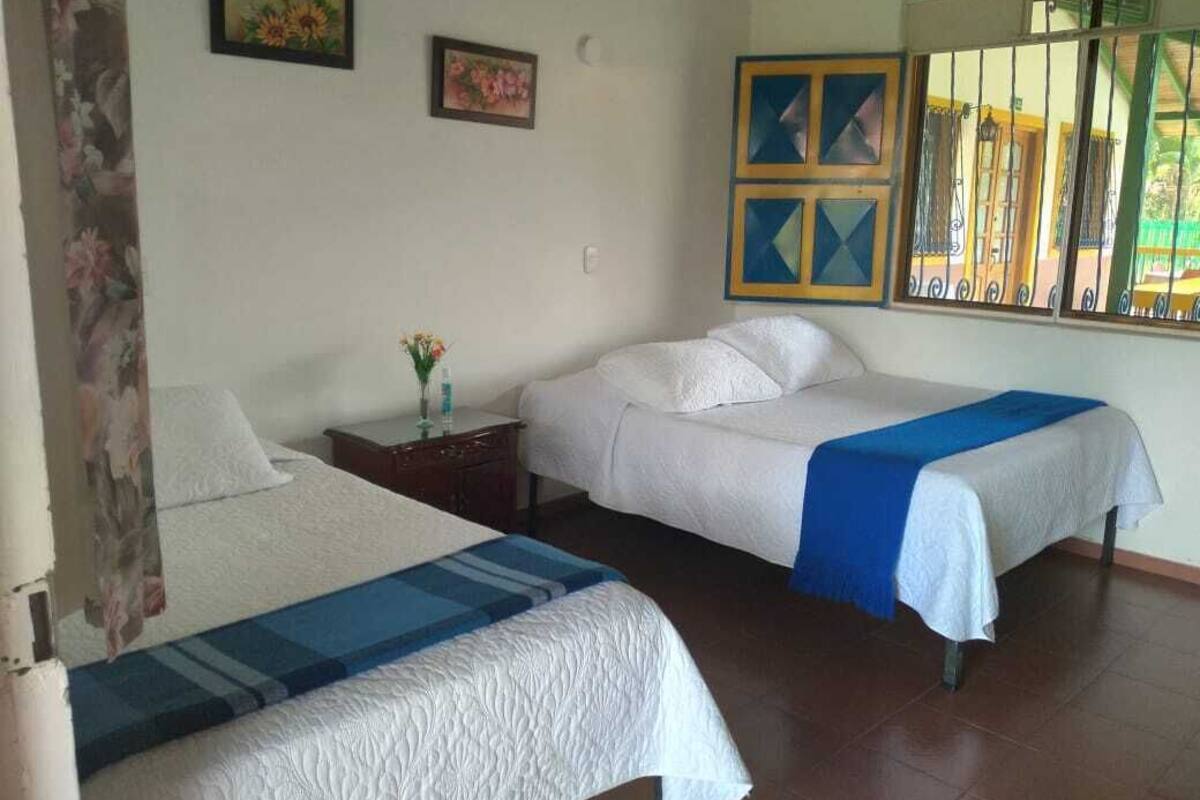 A hotel room with two beds, a nightstand, a vase with flowers, and a window with a view of the outside.