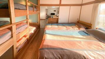 A bunk bed room with a wooden floor, a bed with striped bedding, and a small desk area.
