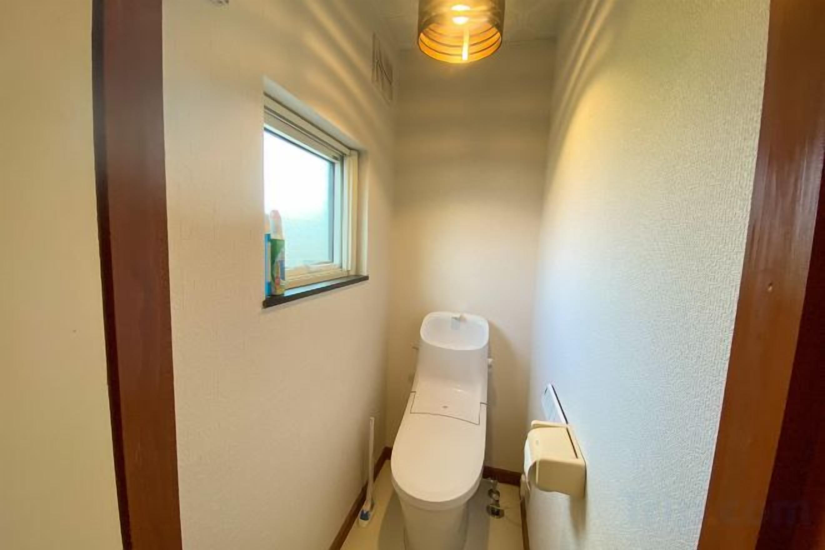 A narrow hallway with a toilet, a window, and a light fixture.