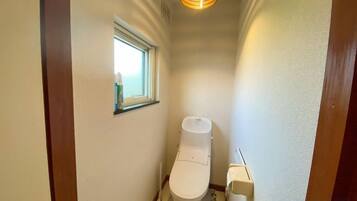 A narrow hallway with a toilet, a window, and a light fixture.