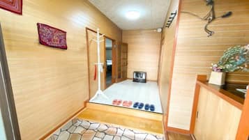 A room with a tatami mat floor, a wooden door, a small table with a plant, and a wall-mounted decoration.