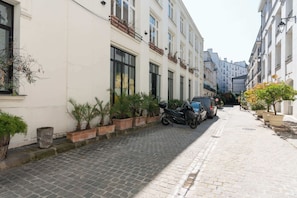 Une rue pavée bordée d’immeubles, de scooters garés et de plantes en pot.