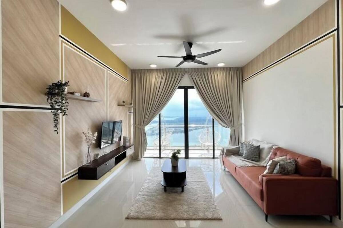 A modern living room with a flat-screen TV, a ceiling fan, a red sofa, and a large window with a view.