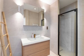 A bathroom with a white sink, wooden vanity, a large mirror, and a glass shower enclosure.