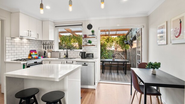A modern kitchen with white cabinetry, a central island with stools, and a dining area with a table and chairs.