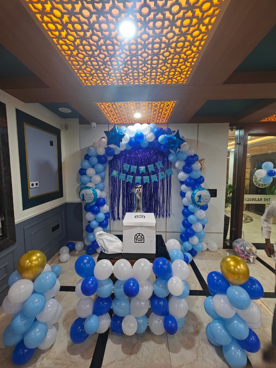 Una habitación con decoración de globos azules y blancos, un trofeo y un cartel que dice '¡Feliz Cumpleaños!'