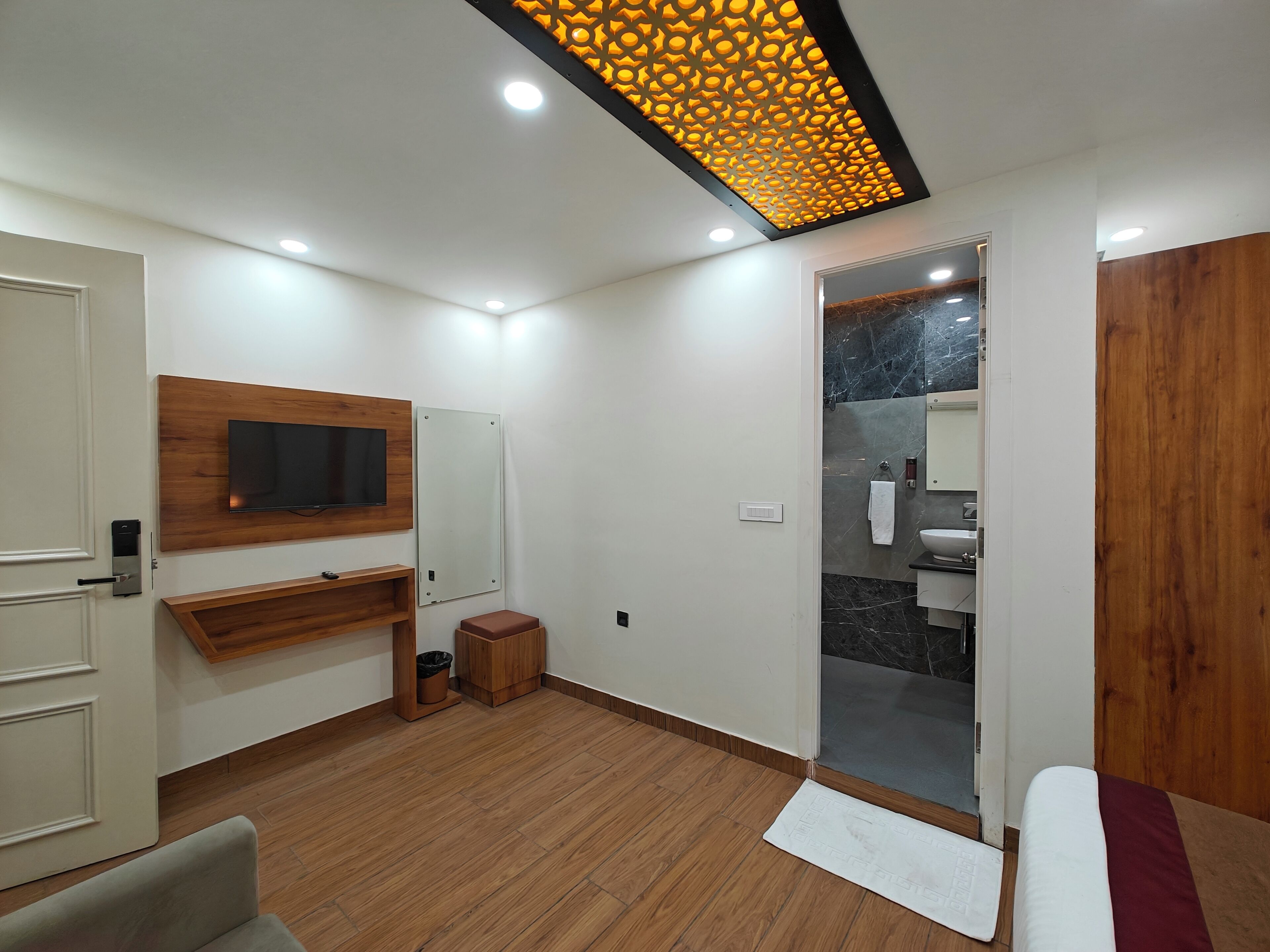 A modern bathroom with a wooden vanity, a mirror, a television mounted on the wall, and a shower area with a marble wall.