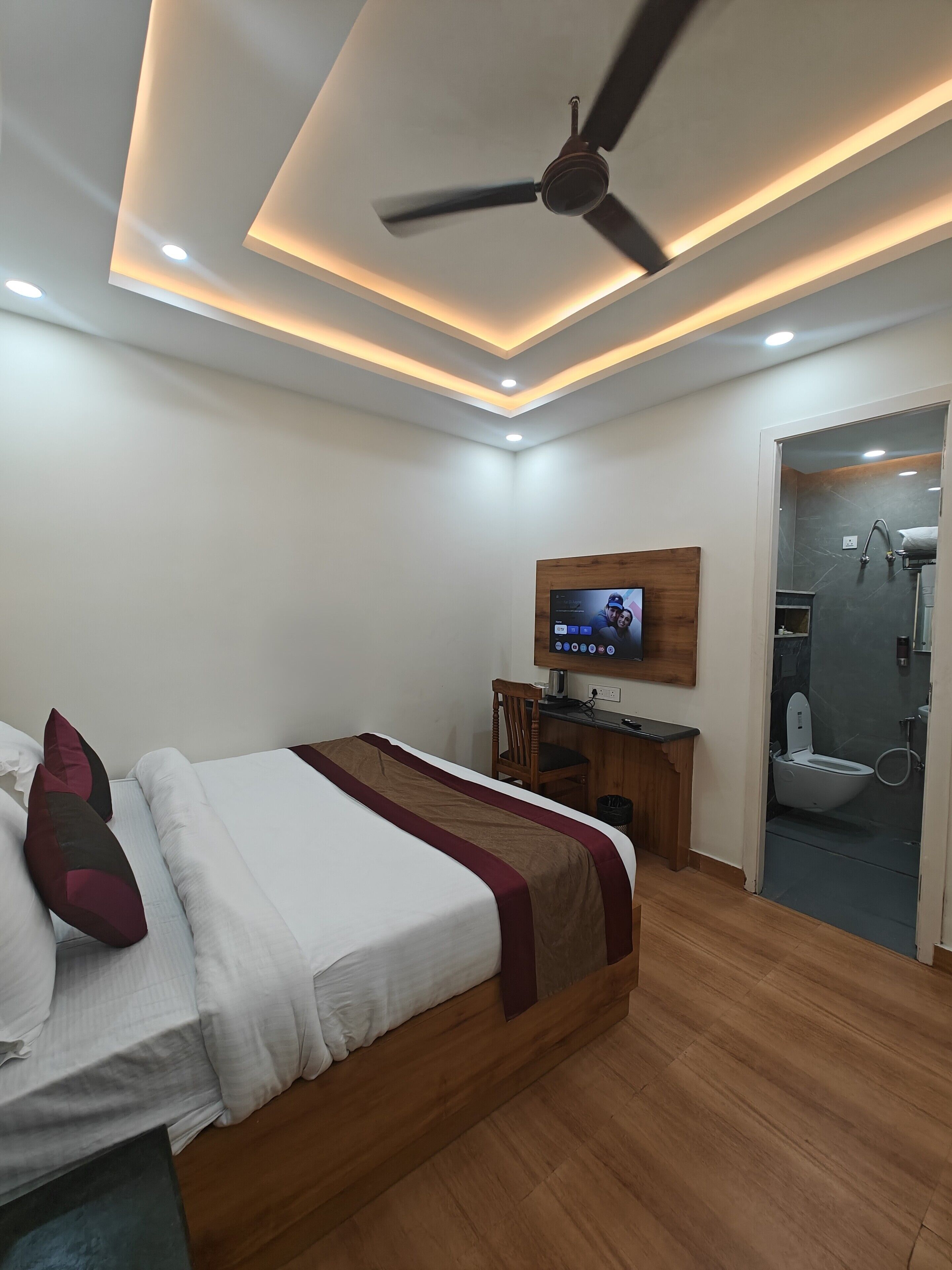 A modern hotel room with a bed, a desk, a television, and a shower area.