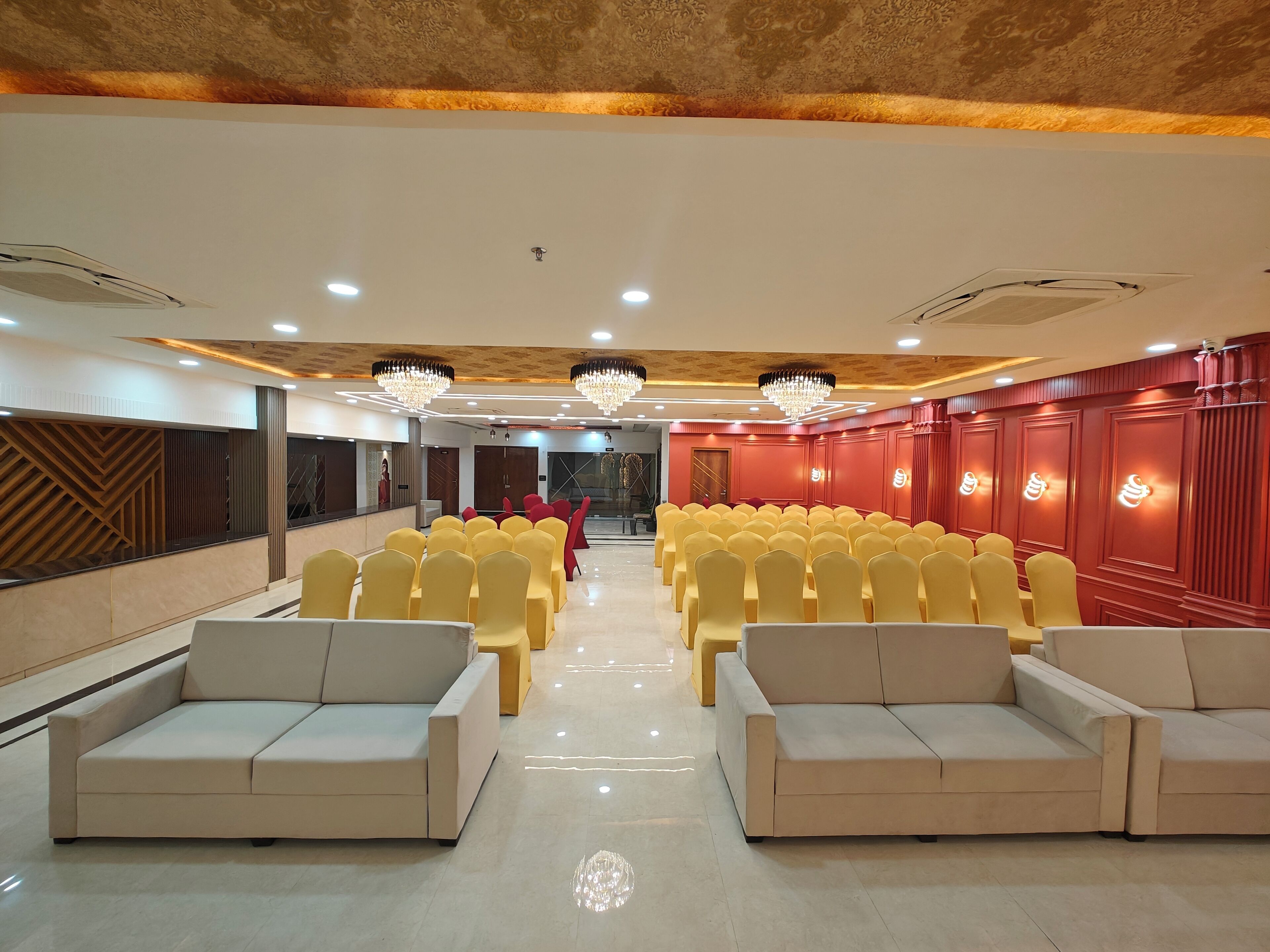 A conference room with rows of yellow chairs and beige sofas, a patterned ceiling, and red wall paneling.