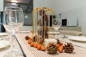Een eettafel met een glazen wijnglas, een wit bord, een gouden decoratieve kooi met dennenappels, en een hartvormige versiering in het wit.